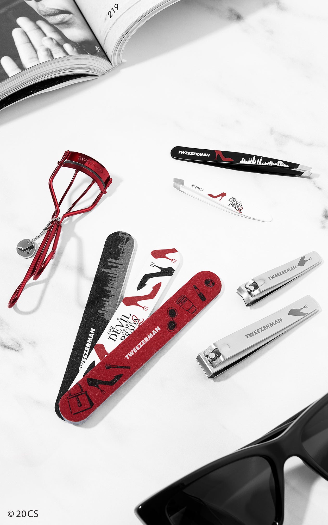 Set of Tweezerman grooming tools on a white surface with sunglasses.