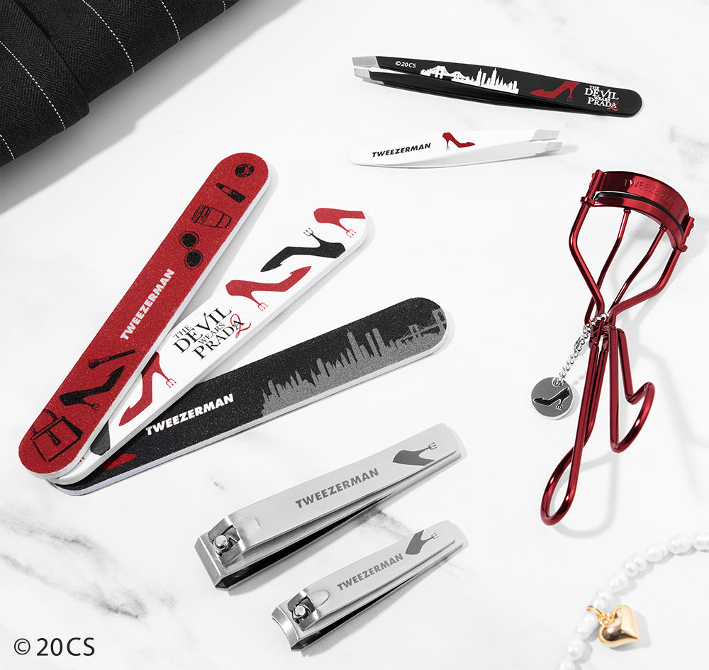 Collection of Tweezerman beauty tools including a red eyelash curler and various the Devil Wears Prada branded nail care tools on a white background.
