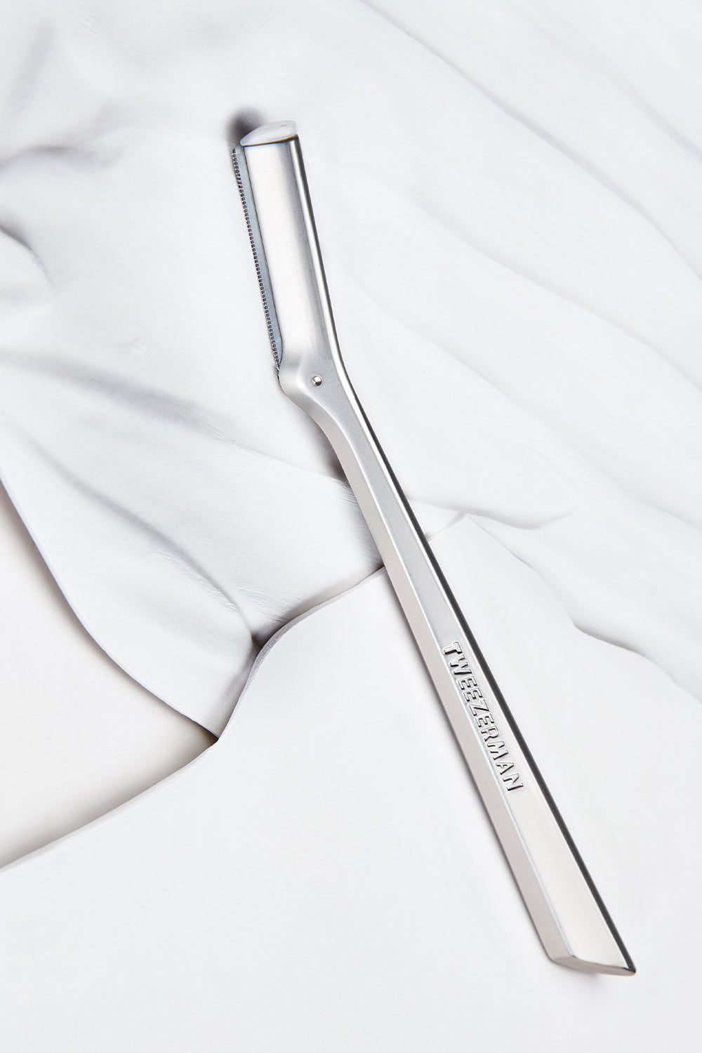 Tweezerman Facial Razor on a white marble background. 
