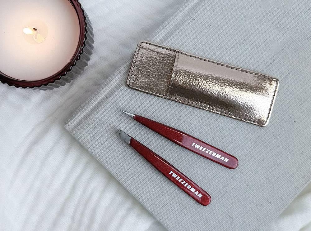 The Vintage Rose Mini Tweezer Set with Case on a book, near a candle