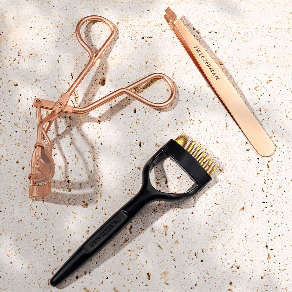 Eyelash Comb, Rose Gold Slant Tweezer and the Rose Gold Eyelash Curler on a pool tile