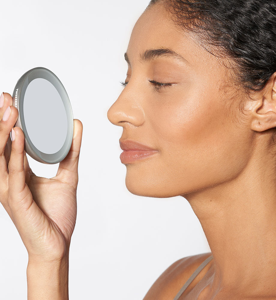 Woman holding a compact mirror to her face against a plain background