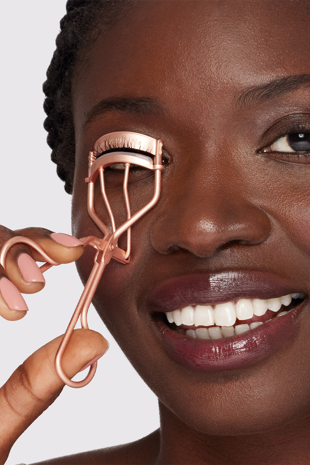 Woman using a rose gold eyelash curler on a plain background