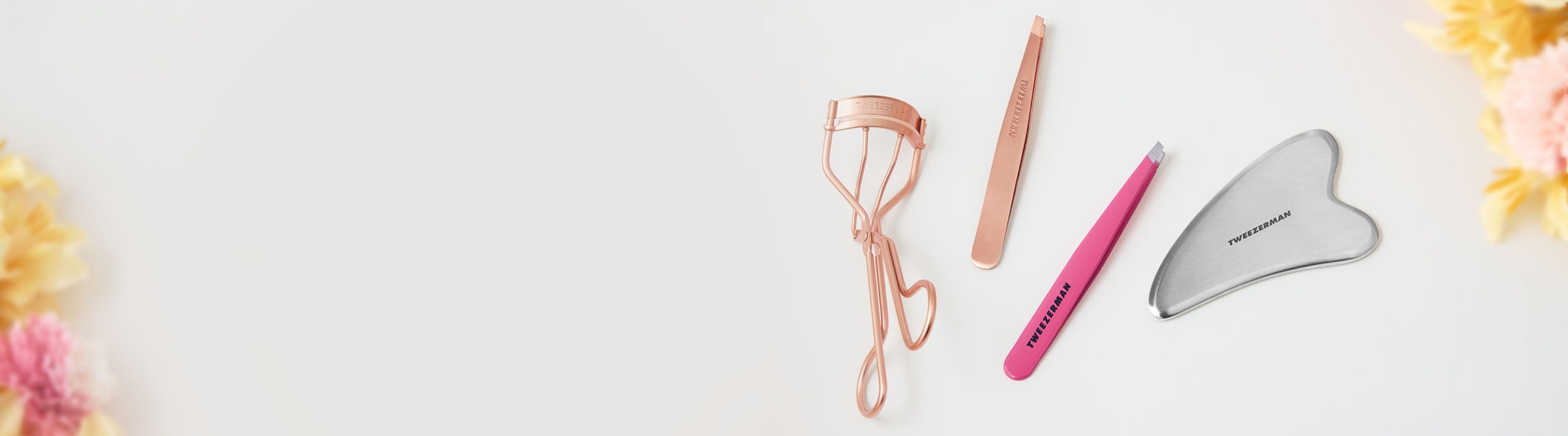 Set of beauty tools including an eyelash curler, tweezers and Gua Sha on a light background.