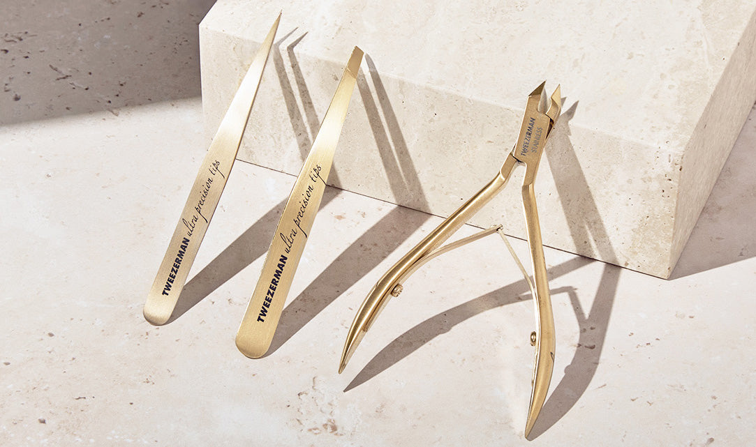 Three gold-toned precision hand tools with engraved text, arranged on a light stone surface beside a matching stone block.