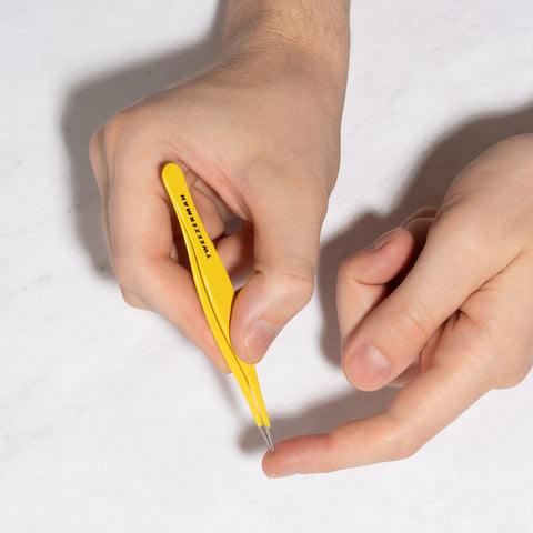 Yellow tweezers being used by a person for splinters on a white background